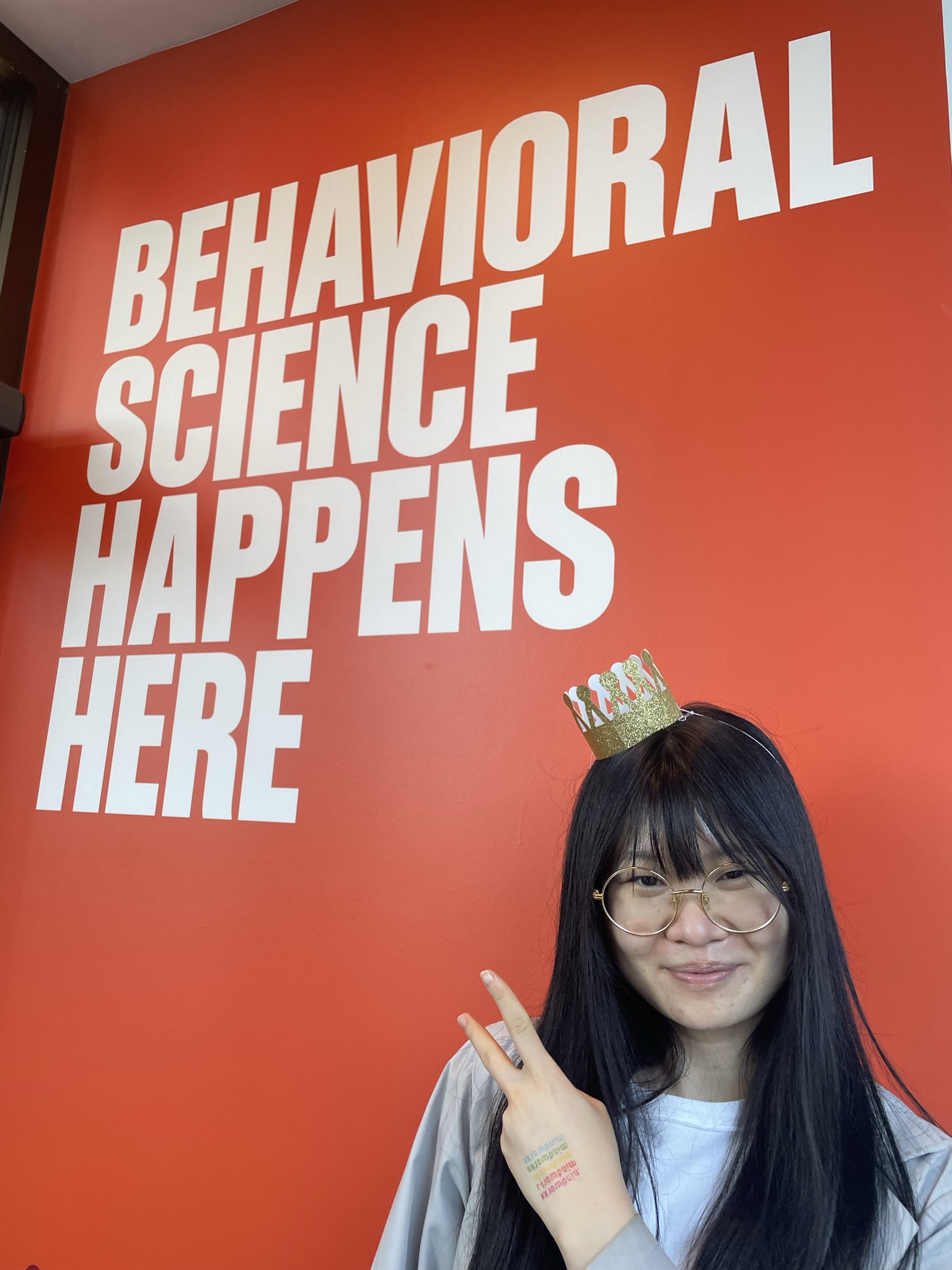 A research assistant poses in front of a wall that says "behavioral science happens here"