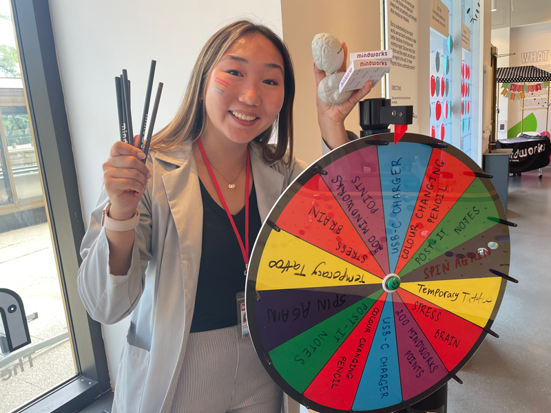 A research assistant poses next to a multi-colored prize wheel